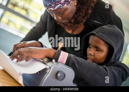 Un insegnante Ester Washinana aiuta i non vedenti allievo di utilizzare una macchina da scrivere braille durante la lezione di inglese a Eluwa scuola speciale in Ongwediva, Namibia Foto Stock