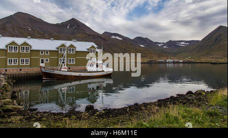 Barca accanto ad un hotel con le montagne sullo sfondo in Siglufjörður, Islanda Foto Stock