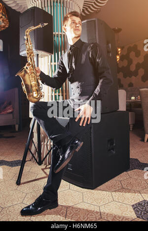 Giovane uomo seduto e tenendo il sassofono Foto Stock