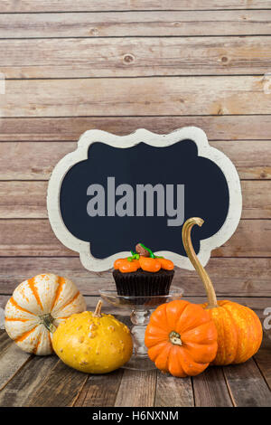 Muffin di zucca con coloquintidi ornamentali e vuoto segno della lavagna Foto Stock