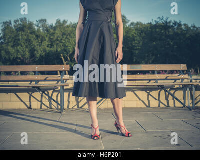 Vintage filtrata colpo di un elegante giovane donna che indossa un abito e in piedi da alcune panchine Foto Stock