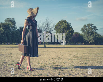 Vintage filtrata colpo di un elegante giovane donna in tacchi alti e un abito a piedi nel parco con una valigetta Foto Stock