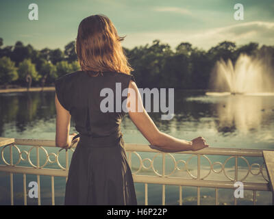 Vintage filtrata colpo di un elegante giovane donna in piedi da un lago in un parco al tramonto Foto Stock