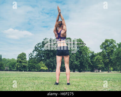 A montare e atletica giovane donna sta lavorando fuori con un hula hoop nel parco su una soleggiata giornata estiva Foto Stock