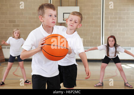 Scuola elementare alunni giocare a basket in palestra Foto Stock