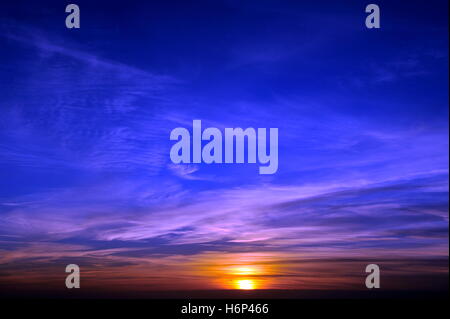 Impostazione sun suddiviso da nuvole di colore arancione su un viola e blu elettrico sky si immerge in mare Foto Stock
