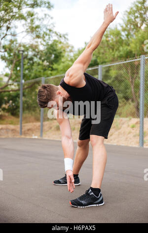 Ritratto di atletica uomo barbuto facendo esercizi di stretching all'aperto Foto Stock