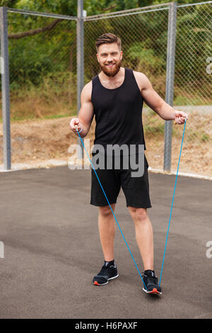 A piena lunghezza Ritratto di un felice barbuto uomo fitness allenamento con salto con la corda all'aperto Foto Stock