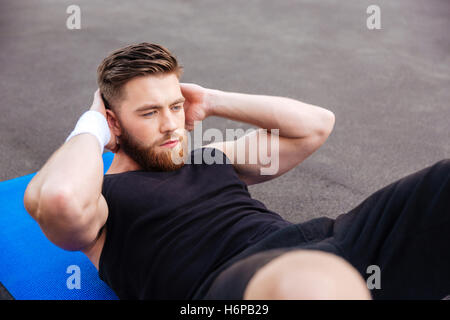 Ritratto di un giovane bello concentrato uomo sportivo facendo premere allenamento sul tappetino fitness all'aperto Foto Stock