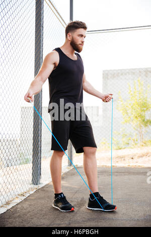 Lunghezza completa di un concentrato uomo fitness facendo esercizi cardio con corda da salto all'aperto Foto Stock