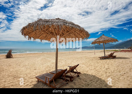 Sedie a sdraio sotto gli ombrelloni di paglia su Lang Co Beach. Thua Thien Huê Provincia, Vietnam. Foto Stock