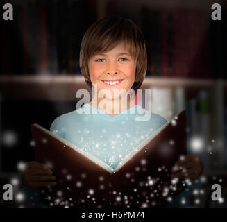 Preteen boy con un libro illuminato lettura in biblioteca Foto Stock