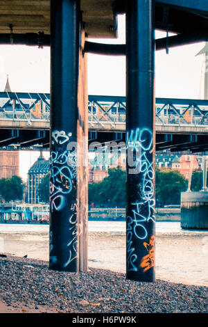 Colonnine di supporto del Festival Pier coperto di graffiti sulla riva della banca del sud del Tamigi a bassa marea, London, Regno Unito Foto Stock
