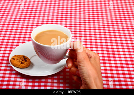 Donna-ladies-ragazze dunking mano un cookie biscotto in una calda tazza di tè con un punto rosso e bianco a scacchi tabella coperta di stoffa Foto Stock