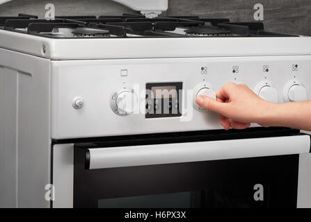 Femmina girando a mano sulla cucina bianca stufa a gas su sfondo grigio Foto Stock