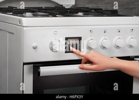 Femmina girando a mano sulla cucina bianca stufa a gas su sfondo grigio Foto Stock