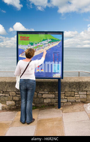 Donna punti turistici a una funzione su un visitatore informazioni mappa sul lungomare che si affaccia sul mare a Teignmouth, Devon Foto Stock