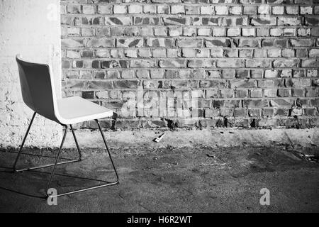 Abstract interno vuoto sfondo bianco, sedia per ufficio sorge su un pavimento di cemento vicino a un muro di mattoni, foto in bianco e nero Foto Stock