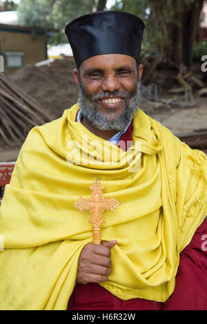 Prete cristiano ortodosso etiope sorridente che tiene una croce etiope, nel cortile della Chiesa di Santa Maria, Kideste Kidusan Maryam, Addis Abeba, Etiopia Foto Stock