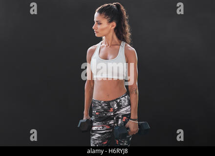Sottile e montare la donna a mano di sollevamento pesi. Femmina muscolare che lavora fuori con manubri su sfondo nero. Modello di bodybuilding doin Foto Stock