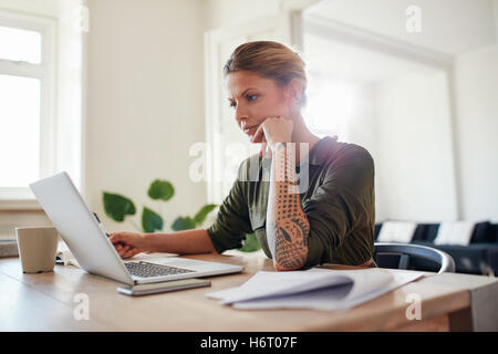 Piscina colpo di giovane donna guardando il laptop sul serio. Donna seduta presso l'ufficio domestico e di lavoro sul computer portatile. Foto Stock