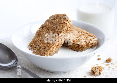 Ciotola bianco con due di tutto il grano biscotti Colazione isolato su bianco con il latte, la bottiglia e il cucchiaio. Le briciole sul cartellone. Foto Stock
