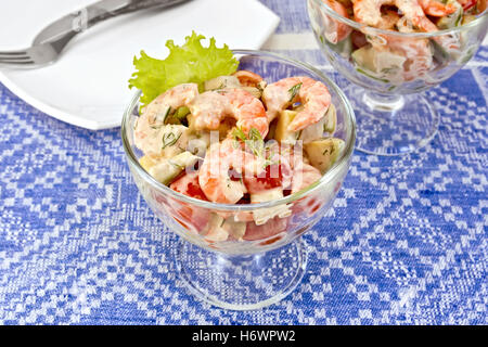 Con insalata di gamberetti, avocado, pomodori, insalata verde in un calice di vetro, una piastra contro lo sfondo di una tovaglia blu Foto Stock