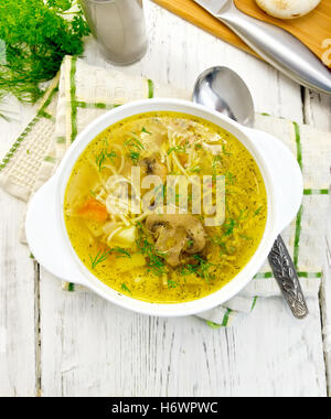 Minestra di pasta e gli champignon in un vaso bianco su un tovagliolo, cucchiaio e pane sullo sfondo di tavole di legno sulla parte superiore Foto Stock