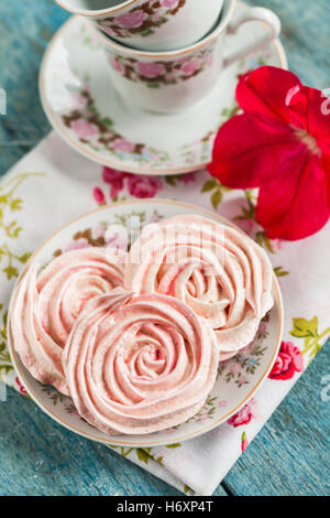 Torte di meringa nella forma delle rose in un romantico piatto con fiore rosso. Foto Stock