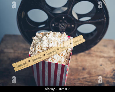 Concetto di cinema della vecchia bobina di pellicola con popcorn e biglietti per il cinema su una superficie in legno Foto Stock
