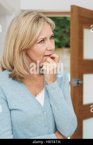 Triste donna matura che soffrono di agorafobia guardando fuori della porta aperta Foto Stock