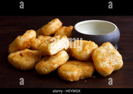 Pila di golden fritte martoriata pepite di pollo con vuoto recipiente rustico in legno scuro. Un taglio di carne che mostra. Foto Stock