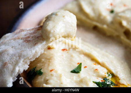 Dettaglio di hummus su pane pita. Piastra del mangiato hummus in background. Foto Stock