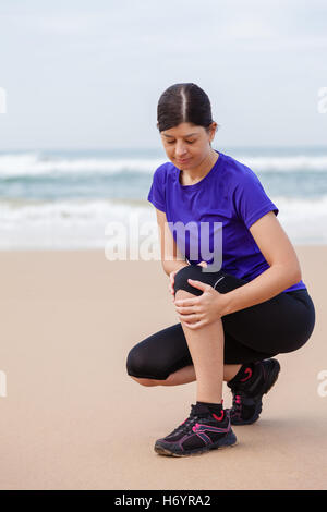 Atleta femminile soffre di un infortunio al ginocchio in spiaggia in una giornata autunnale. Foto Stock