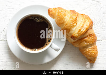 Il croissant e caffè sul rustico in legno bianco, dall'alto. Foto Stock