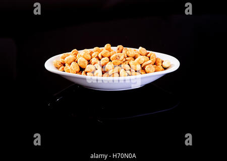 Arrosto di arachidi salate in una piastra bianca su sfondo nero Foto Stock