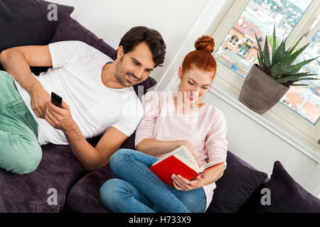 Gli amanti della giovane coppia in soggiorno sul divano mentre la lettura e la visione TV Foto Stock