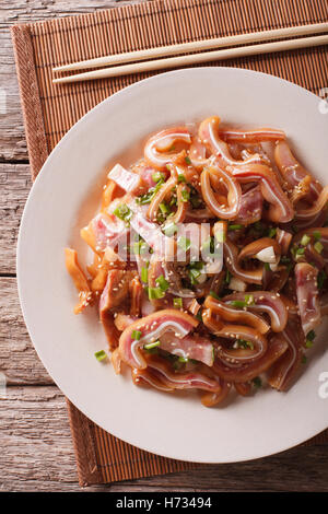 Carne di maiale piccante orecchie con semi di sesamo e le cipolle verdi close-up su una piastra sul tavolo. vista verticale da sopra Foto Stock