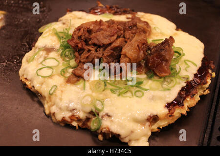 Okonomiyaki, Giapponese Pizza conditi con formaggio, cipolla verde e carni bovine sulla piastra di ferro calda a Kyoto, Giappone Foto Stock