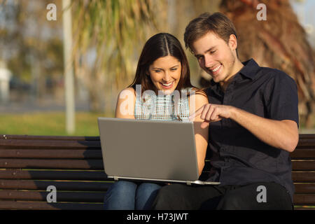 Giovane guardare i media in un notebook seduta su una panchina Foto Stock