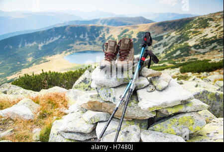 Scarponi e bastoncini da trekking sul picco di montagna e lago sullo sfondo Foto Stock