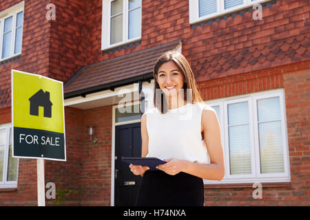 Agente immobiliare femmina in piedi al di fuori di immobili residenziali Foto Stock