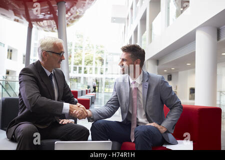 Due imprenditori stringono le mani nella lobby dell ufficio moderno Foto Stock