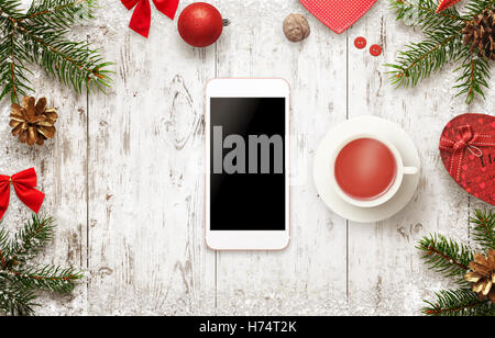 Smart phone con decorazioni di Natale sulla tavola. Bere il tè e una pausa nelle giornate invernali. Visualizzazione isolata del dispositivo mobile Foto Stock
