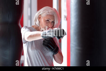 Concentrato piuttosto grigio donna dai capelli il pugilato in una palestra. Foto Stock