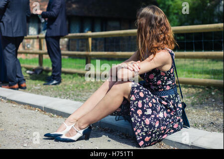 Una giovane donna che indossa un abito è seduto fuori su una fattoria con ben vestiti persone che partecipano a un evento sociale o raccogliere Foto Stock