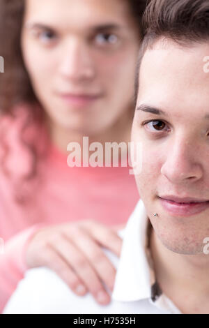 Ritratto di giovane a pelo corto gay uomo guardando a voi mentre il suo fidanzato lo supporta sfocati sullo sfondo Foto Stock