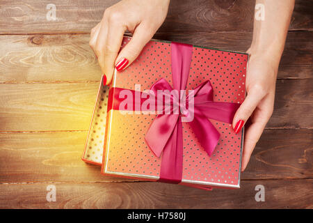 Mani femminili aprendo il Natale o il giorno di san valentino confezione regalo al di sopra di un tavolo di legno. Vista superiore Foto Stock