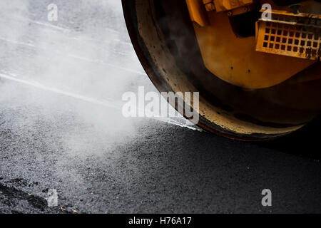 Asfaltatura con una ruota in acciaio rullo. Il vapore uscente dall'asfalto. Foto Stock