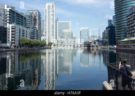 Un uomo non identificato di scattare foto di Millwall Inner Dock con South Quay e Canary Wharf in background da Glengall Bridge. Foto Stock